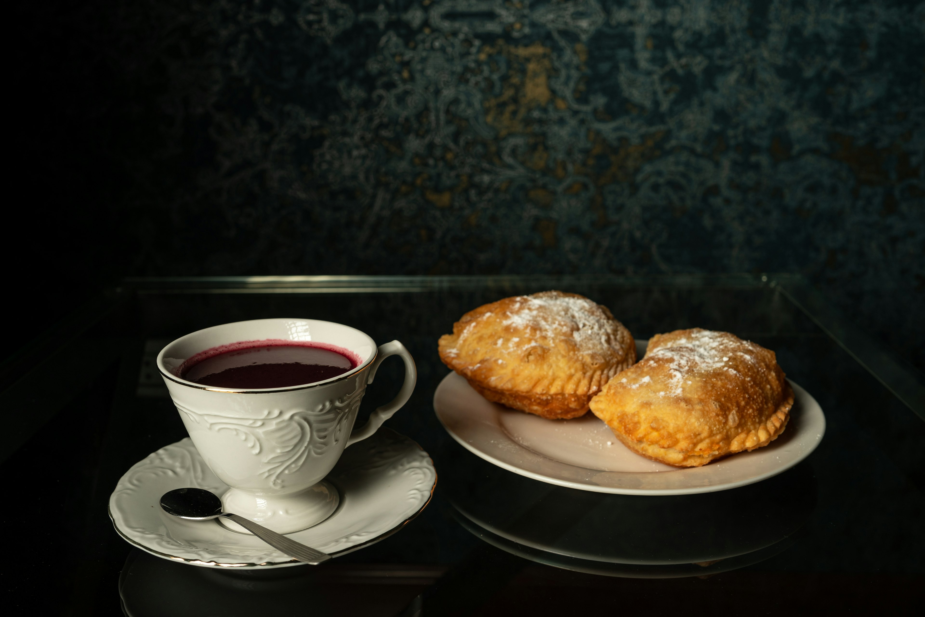 Fried empanadas sit on a plate next to a cup of api de maíz morado