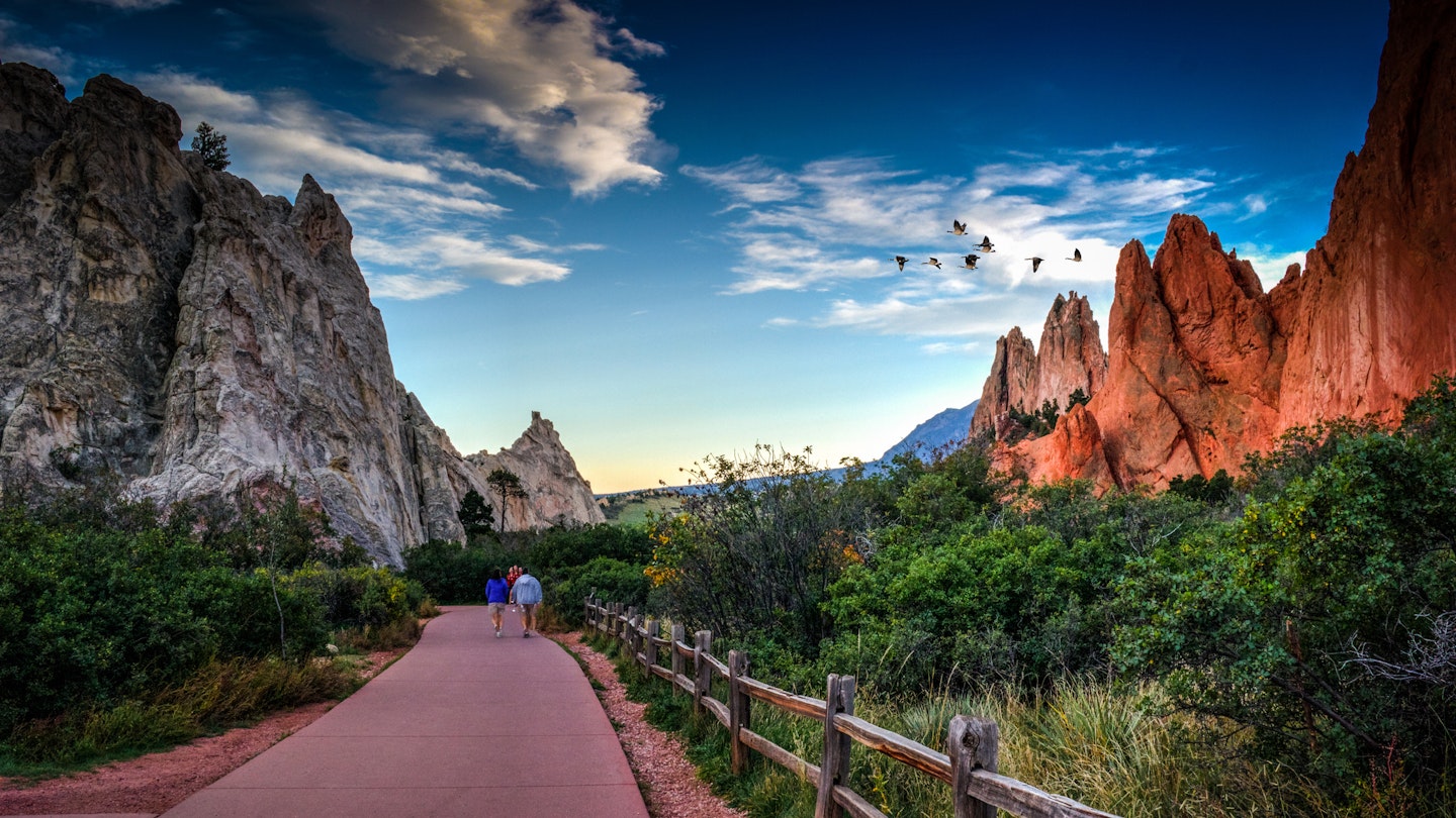 Rear View Of People Walking On Footpath By Rock Formation And Plants Against Sky At Colorado Springs - stock photo
