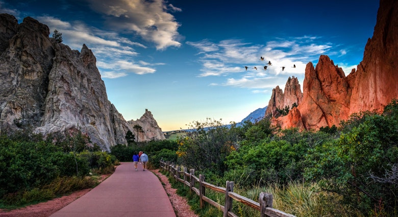 Rear View Of People Walking On Footpath By Rock Formation And Plants Against Sky At Colorado Springs - stock photo

