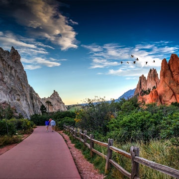 Rear View Of People Walking On Footpath By Rock Formation And Plants Against Sky At Colorado Springs - stock photo
