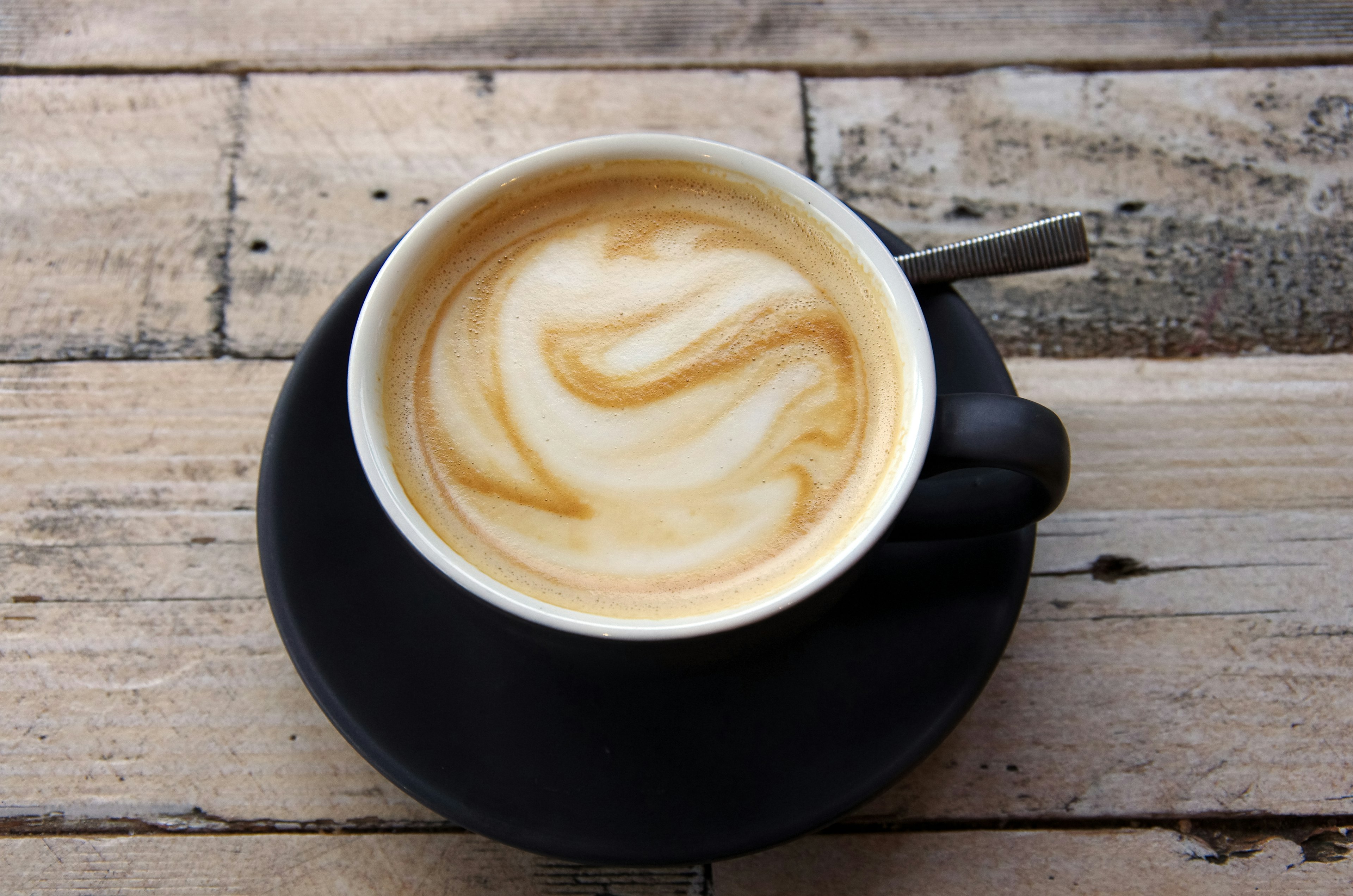 Flat white coffee in a black cup and saucer on a wooden cafe table