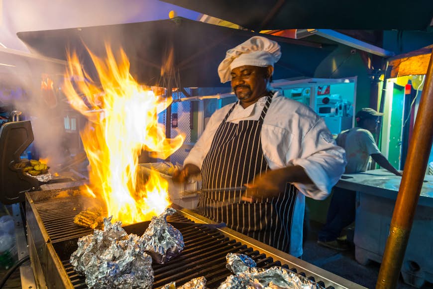 A chef barbecues some fish wrapped in tin foil on a grill