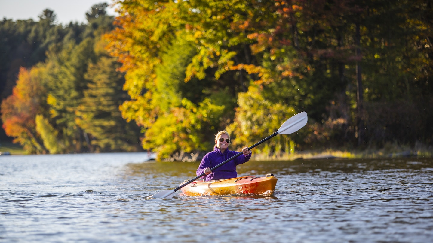 Woman kayaking on a lake during peak foliage, Silver Lake, Vermont.