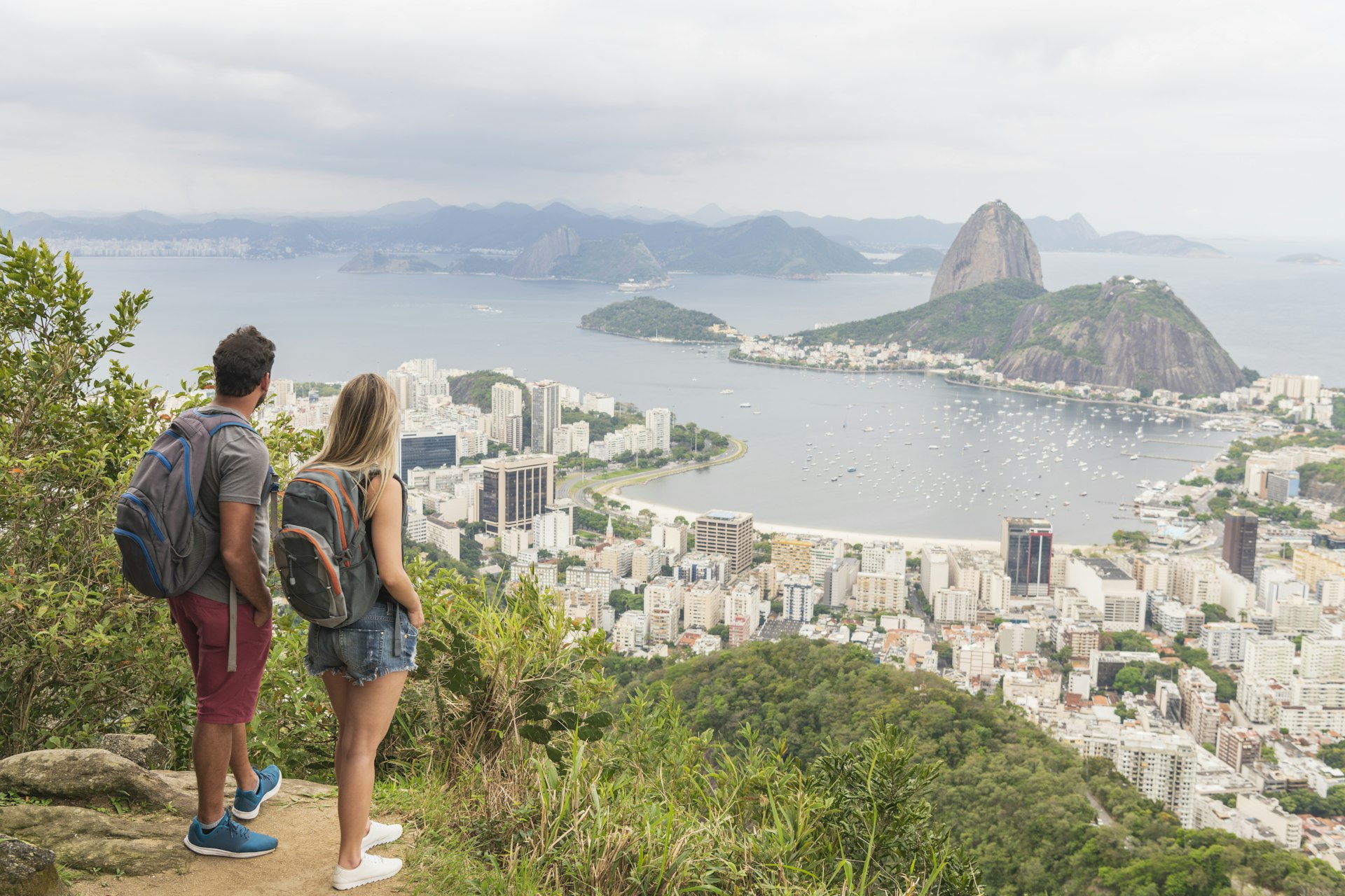 Elevated shot of two backpacking tourists, standing and looking at the view of Sugar Loaf Mountain in Rio de Janeiro, Brazil