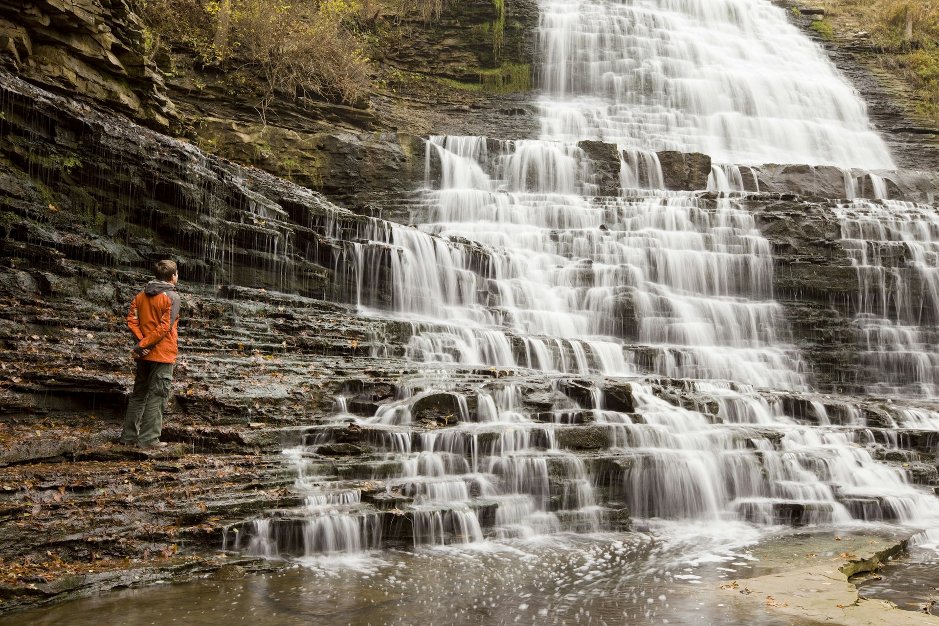 A hiker stands next to a cascade that is splashing off tiered rocks
