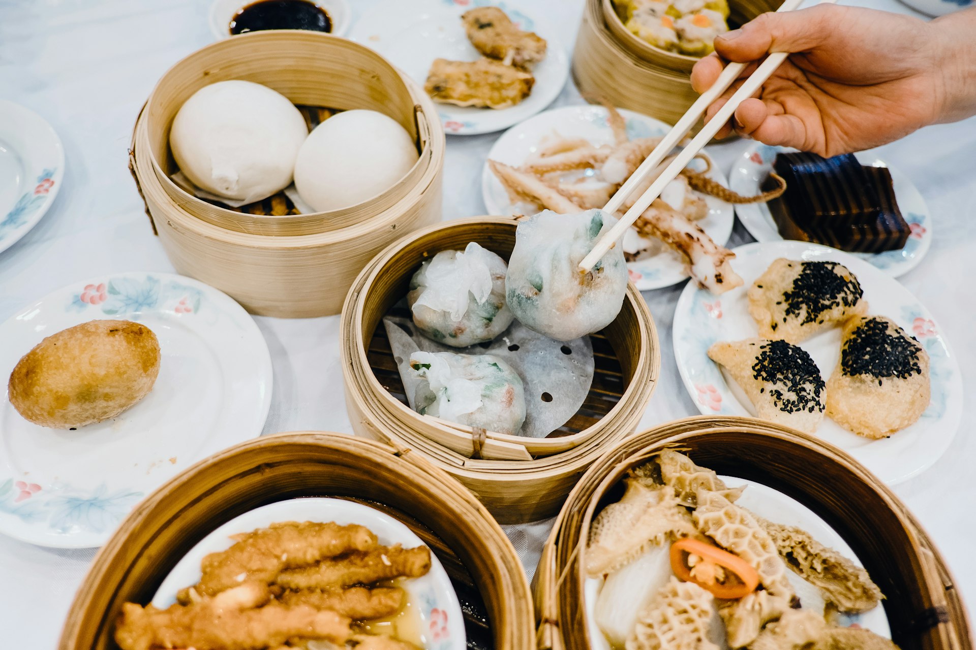 Close up of human hands picking up steamed dumpling with chopsticks and enjoying a variety of traditional dim sum in Chinese restaurant 