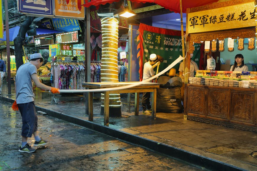 Неизвестный мужчина делает лапшу ручной работы в продовольственном магазине в дождливый день в мусульманском квартале Сиань, Китай.