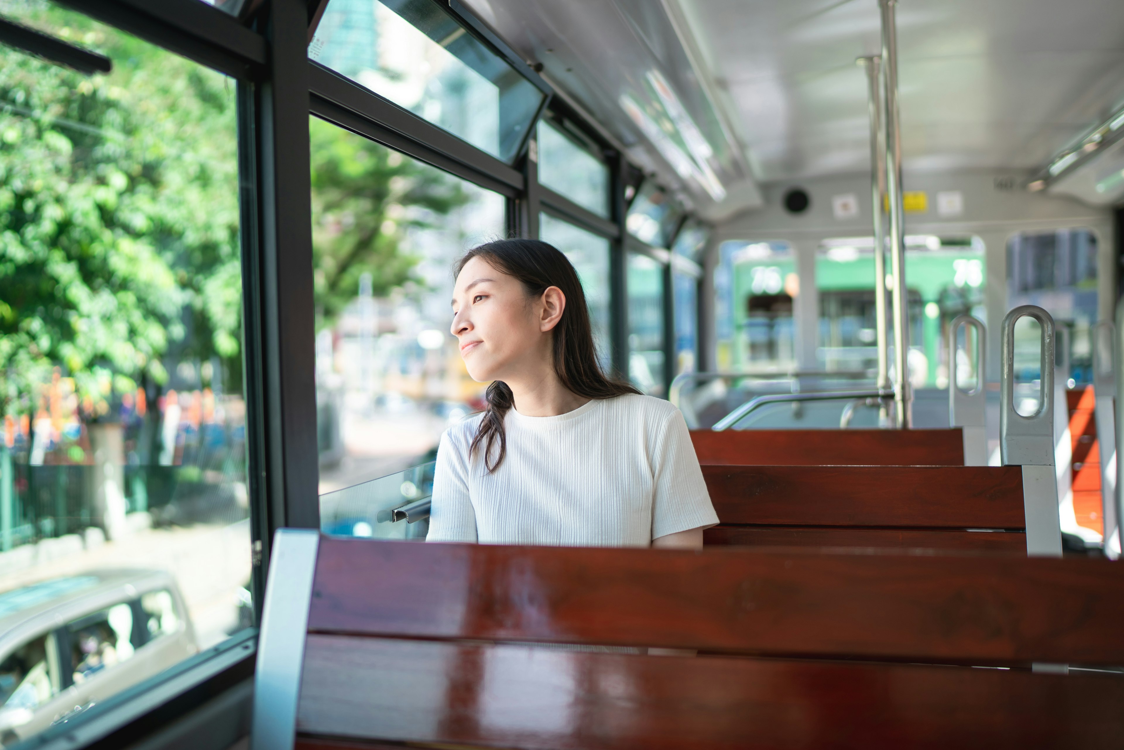 A smiling young tourist woman sits on double decker tram in Hong Kong on a sunny day