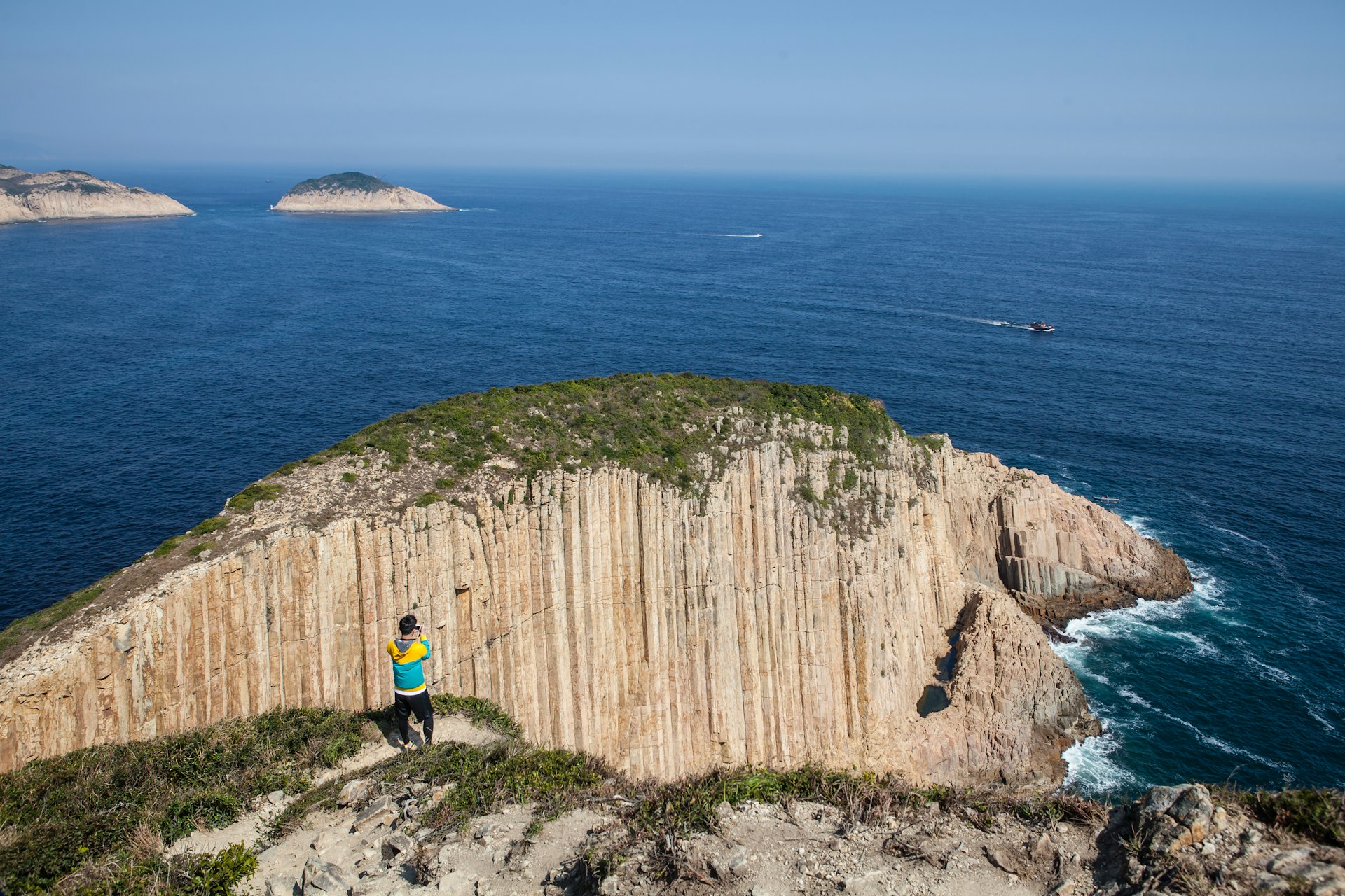 Person taking a photo of a cliff and the ocean at Hong Kong Global Geopark on a sunny day