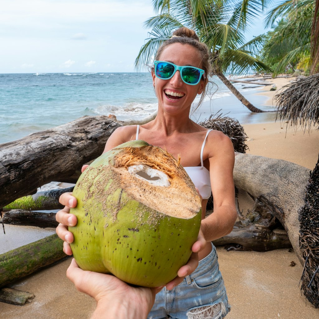 Young couple sharing a coconut on beautiful tropical beach in Costa Rica. Two people, man's pov giving coco to girlfriend