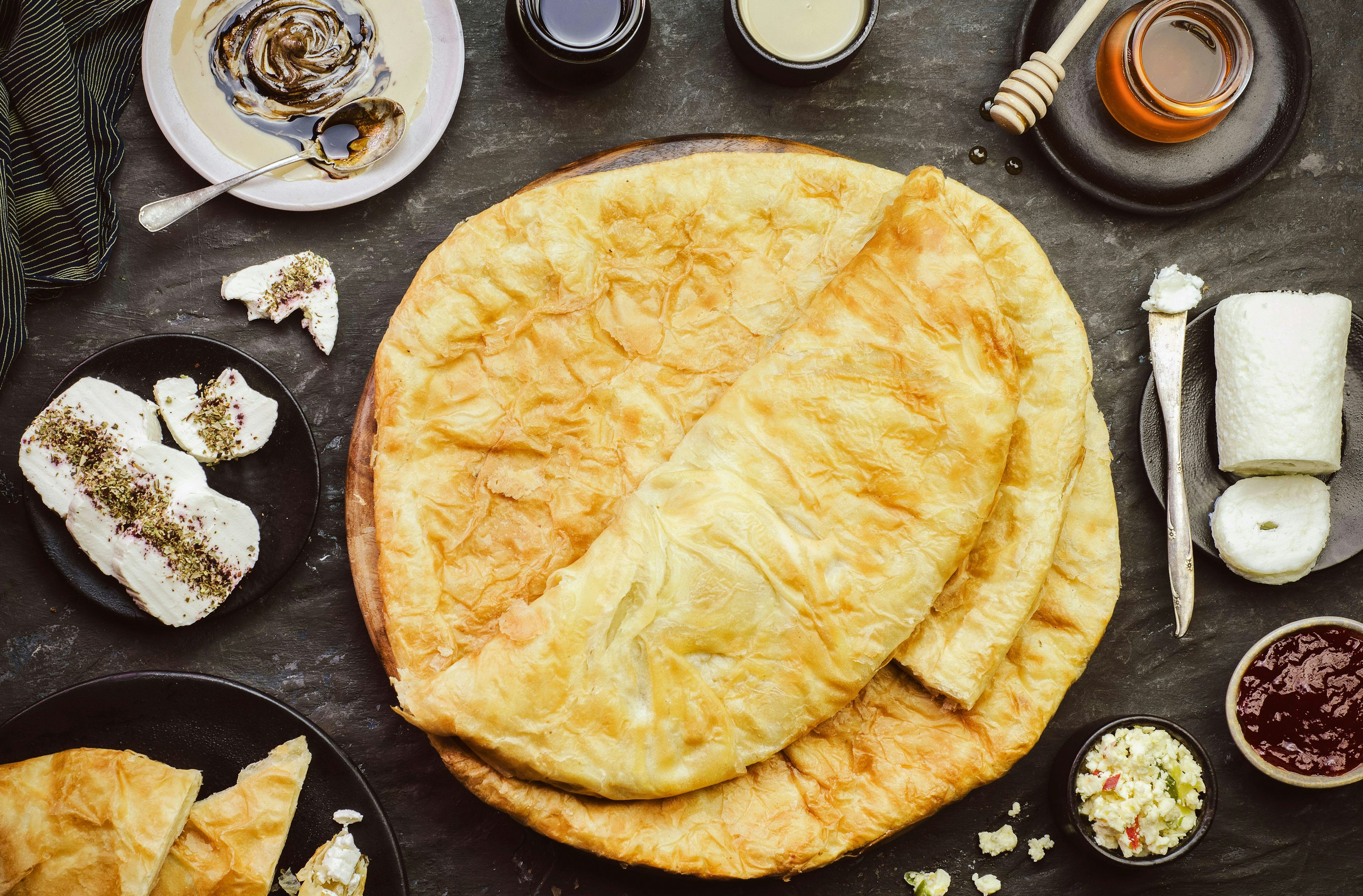 A plate of feteer, a flaky layered pastry popular in Egypt, on a table surrounded by bowls of honey, cheese and other ingredients