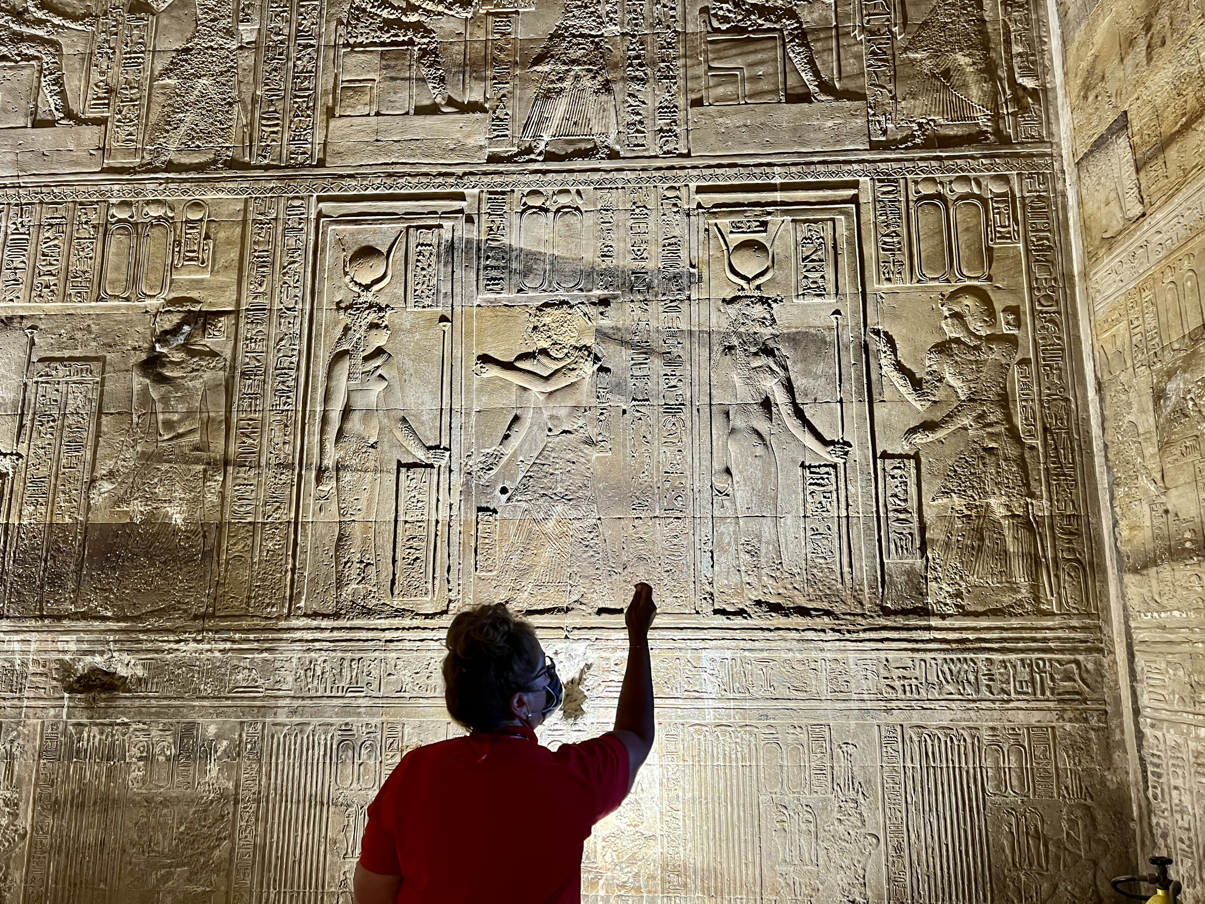 An expert points out markings on a wall and explains them to tourists on a guided tour