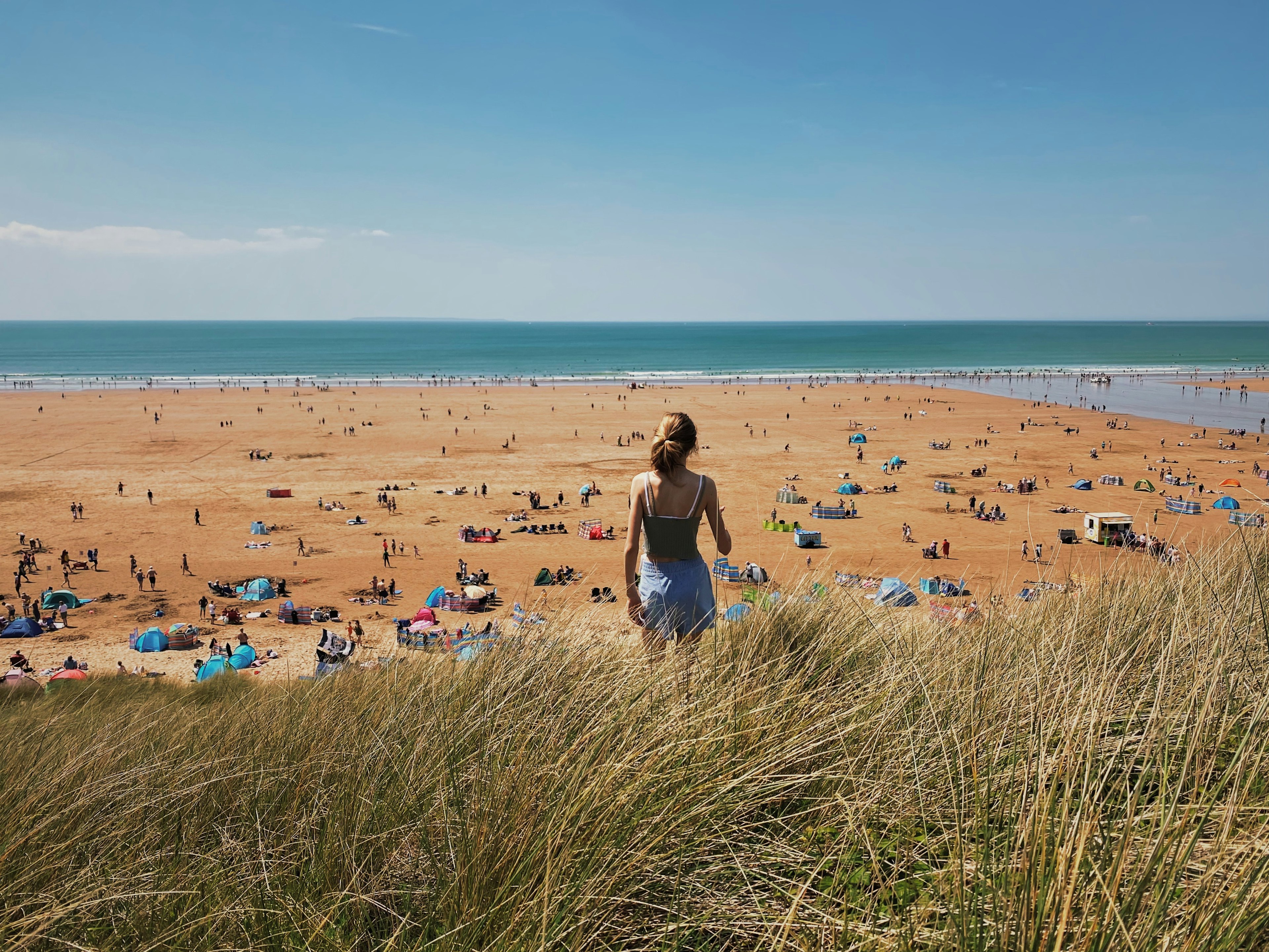 Rear view of a girl on vacation looking out onto a busy beach in Devon