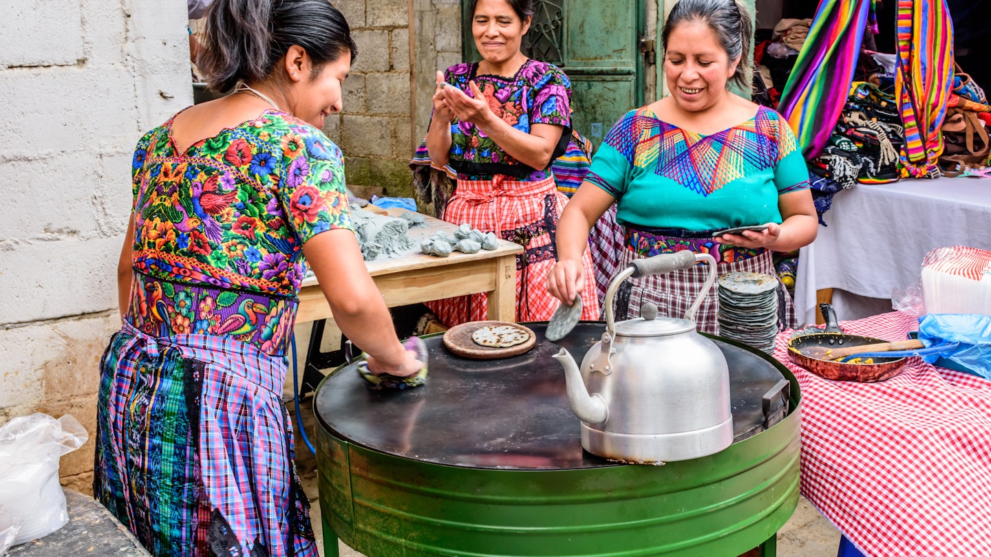 Local Maya women dressed in traditional clothing make corn tortillas in the street during the giant kite festival on All Saints' Day.