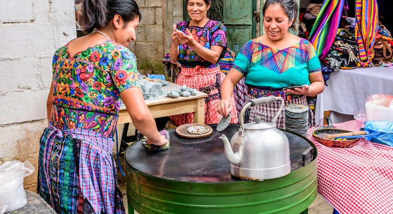Local Maya women dressed in traditional clothing make corn tortillas in the street during the giant kite festival on All Saints' Day.