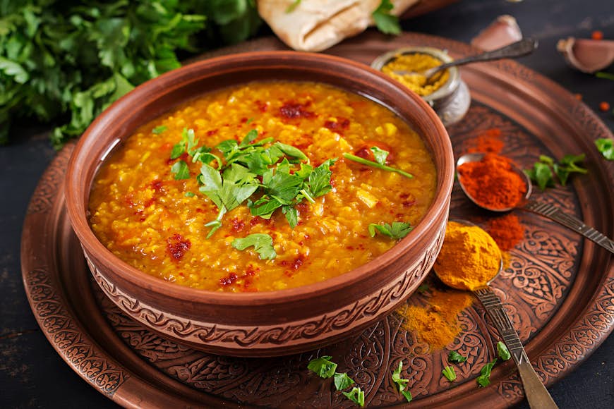 Indian dal, a traditional Indian curry made from lentils, in a bowl with spices, herbs, and a rustic black wooden background.