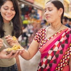 Happy Indian mother, daughter and son eating street food (Bhelpuri) together in outdoor market at day time.