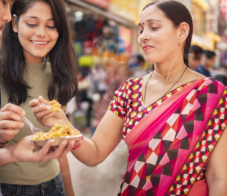 Happy Indian mother, daughter and son eating street food (Bhelpuri) together in outdoor market at day time.
