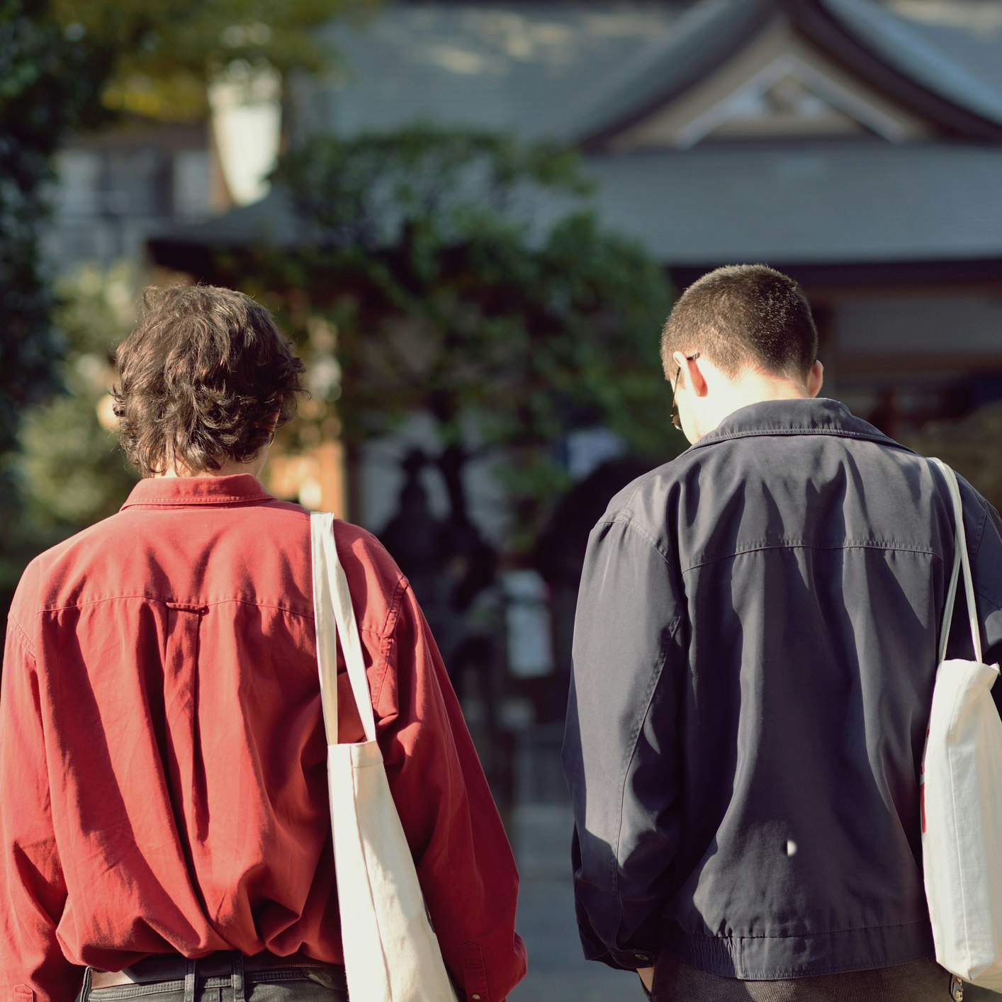 Two young men walking towards a shinto shrine on a sunny day.