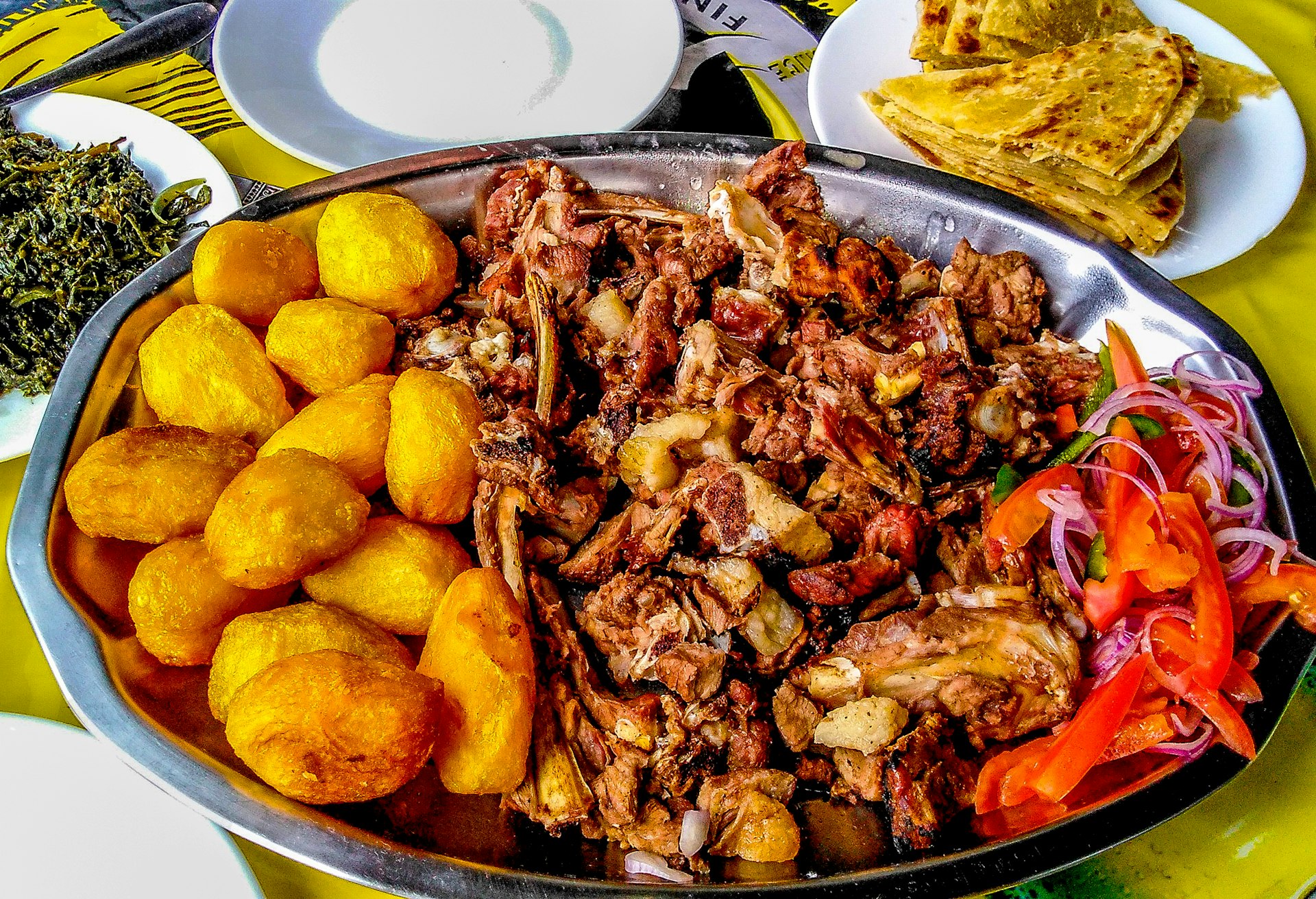 Sharing platter of a traditional Kenyan dish, Nyama choma and accompaniments of kachumbari salad, sukuma wiki, chapati and roast potatoes.