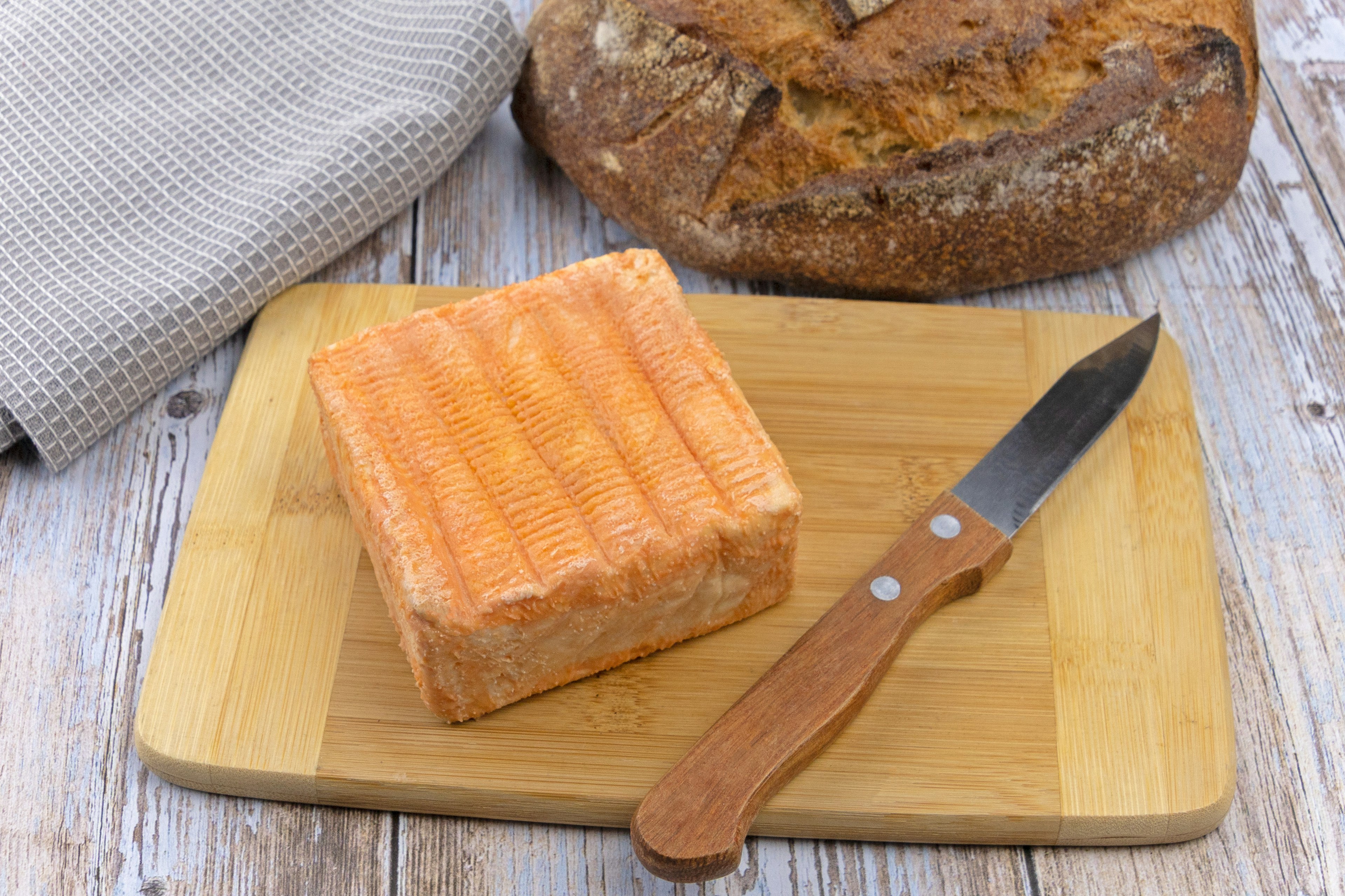 A square of yellow maroilles cheese on a cutting board.