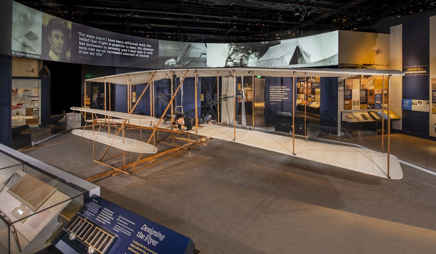 A historic Wright flyer plane sits in a museum hall. 