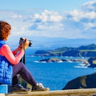 Woman with camera take travel picture from sea landscape, Atlantic ocean and Asturias coast at Cape Penas in north Spain.; Shutterstock ID 2177193009; your: Ben N Buckner; gl: 65050; netsuite: Online Editorial; full: Asturias Northern Spain Sponsored