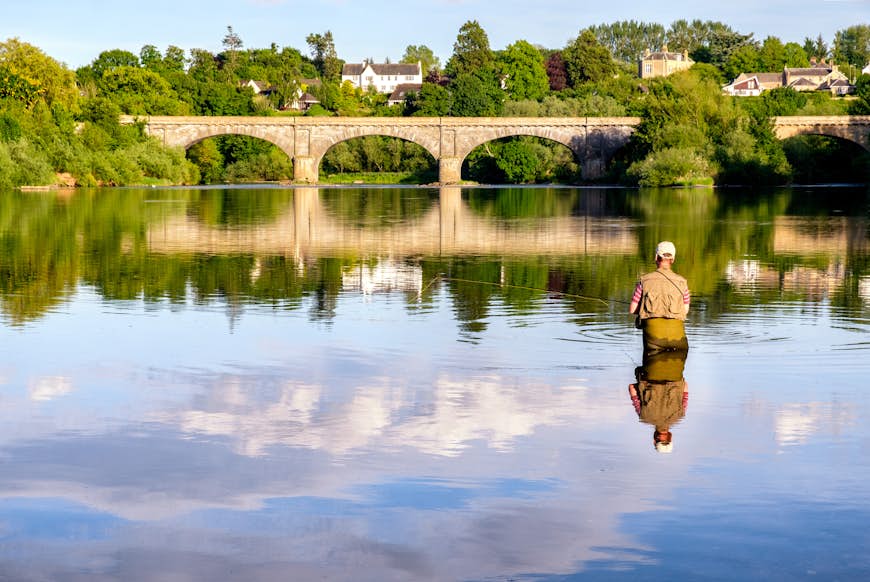 Man fly-fishing on the River Tweed with the iconic Kelso Bridge at the background. Kelso, Scottish Borders, Scotland, UK
