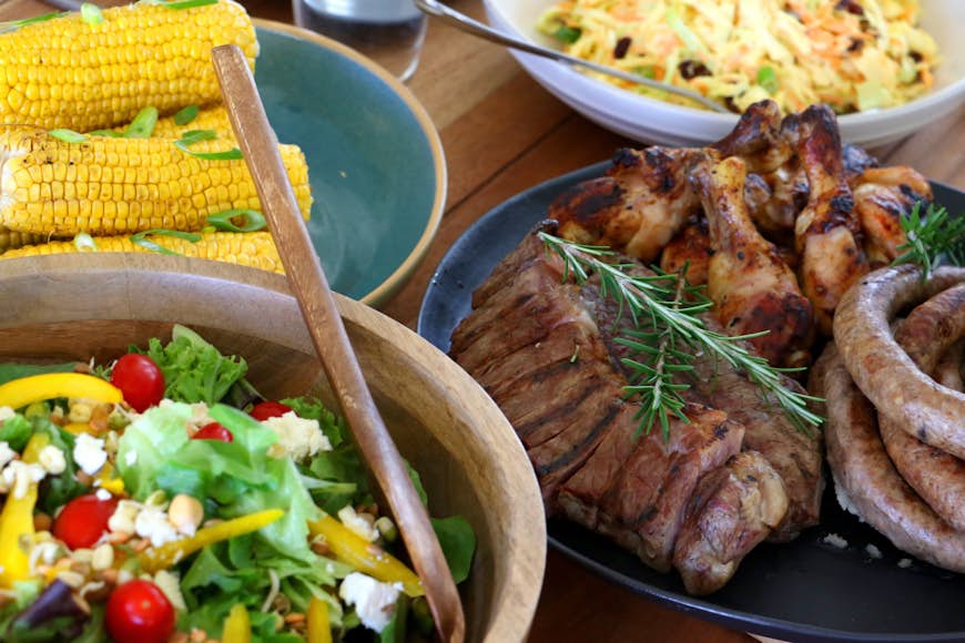 Colorful barbecue braai: plates containing chicken, steak, boerewors salad and coleslaw, laid out and ready to eat on table