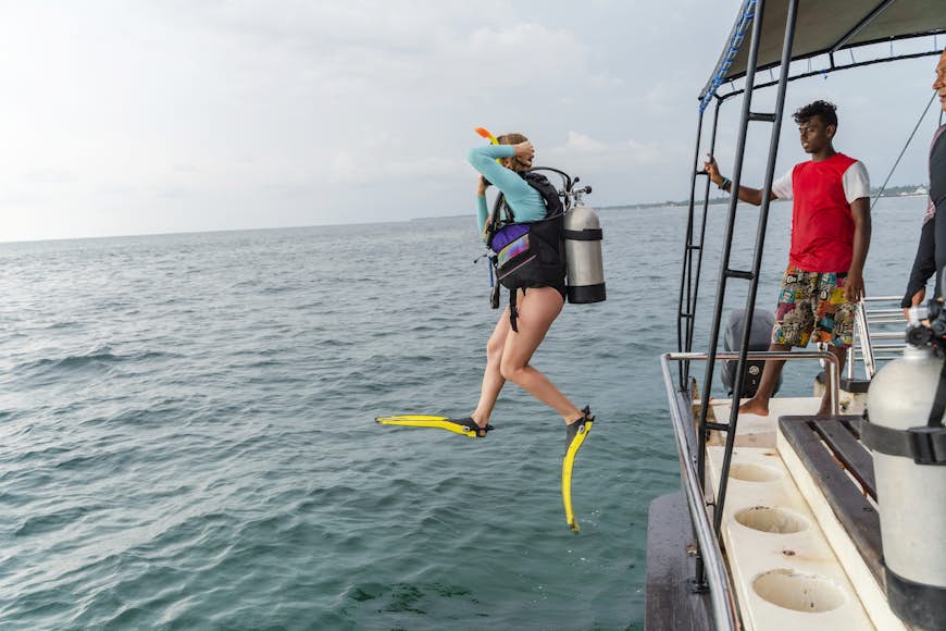 A woman diver wearing a diving suit and aqualung, jumping into the ocean from a boat in Hikkaduwa, Sri Lanka