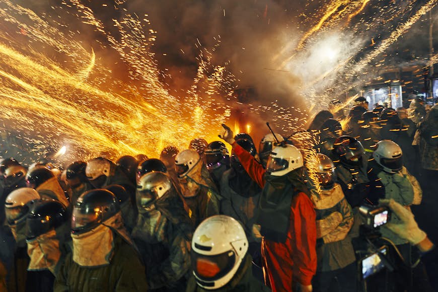 People crowded together wearing crash helmets and other protective gear as fireworks spark around them