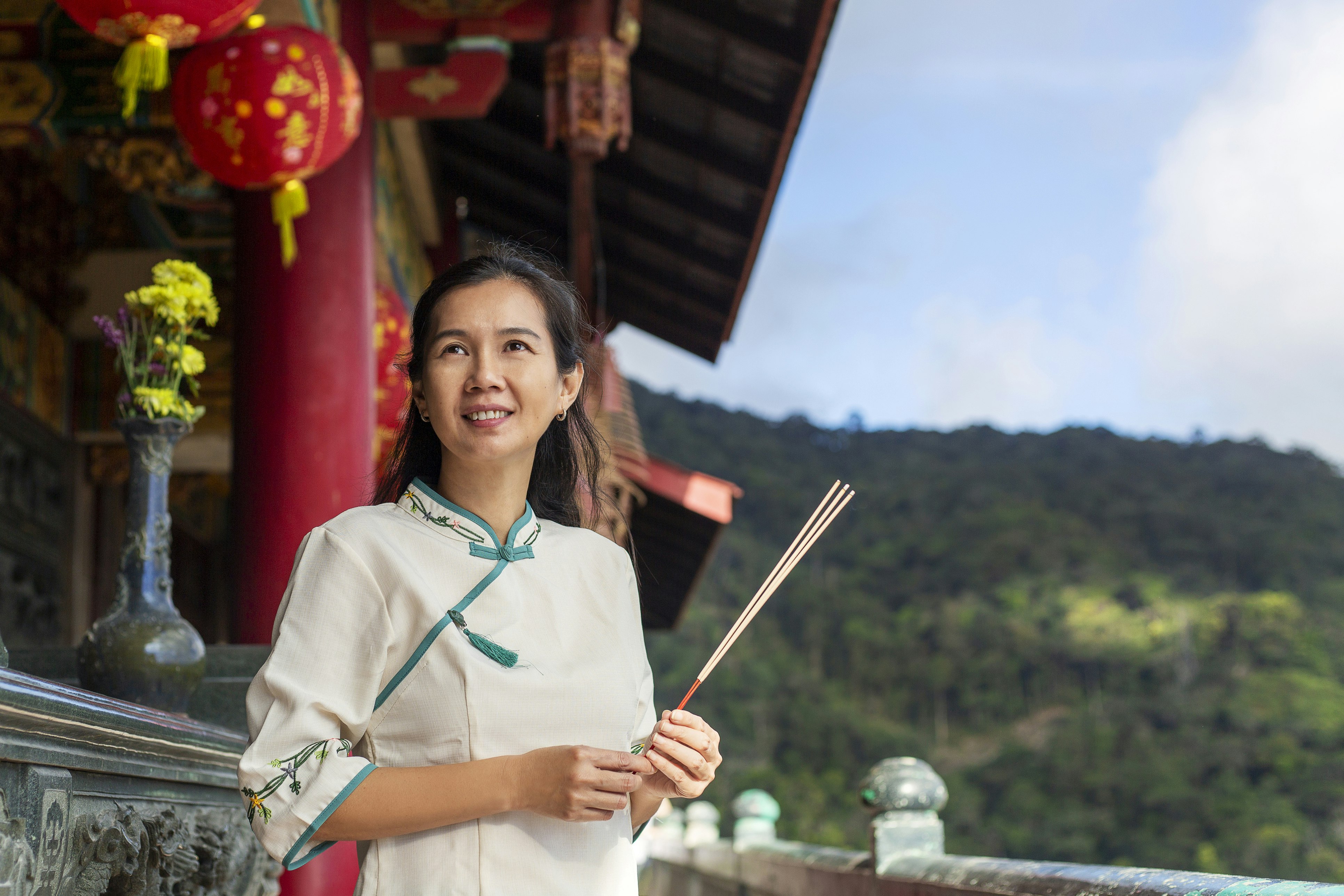 Asian woman holding incense stick outside of a Chinese temple