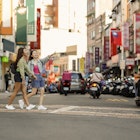 Two young Asian women come to Taipei Tamsui Old Street for independent travel in summer, with pedestrians and land motorcycle traffic in the background of old street market