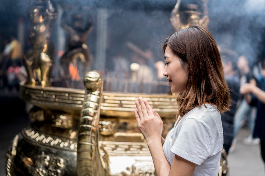 An Asian woman prays and bows her head in a temple