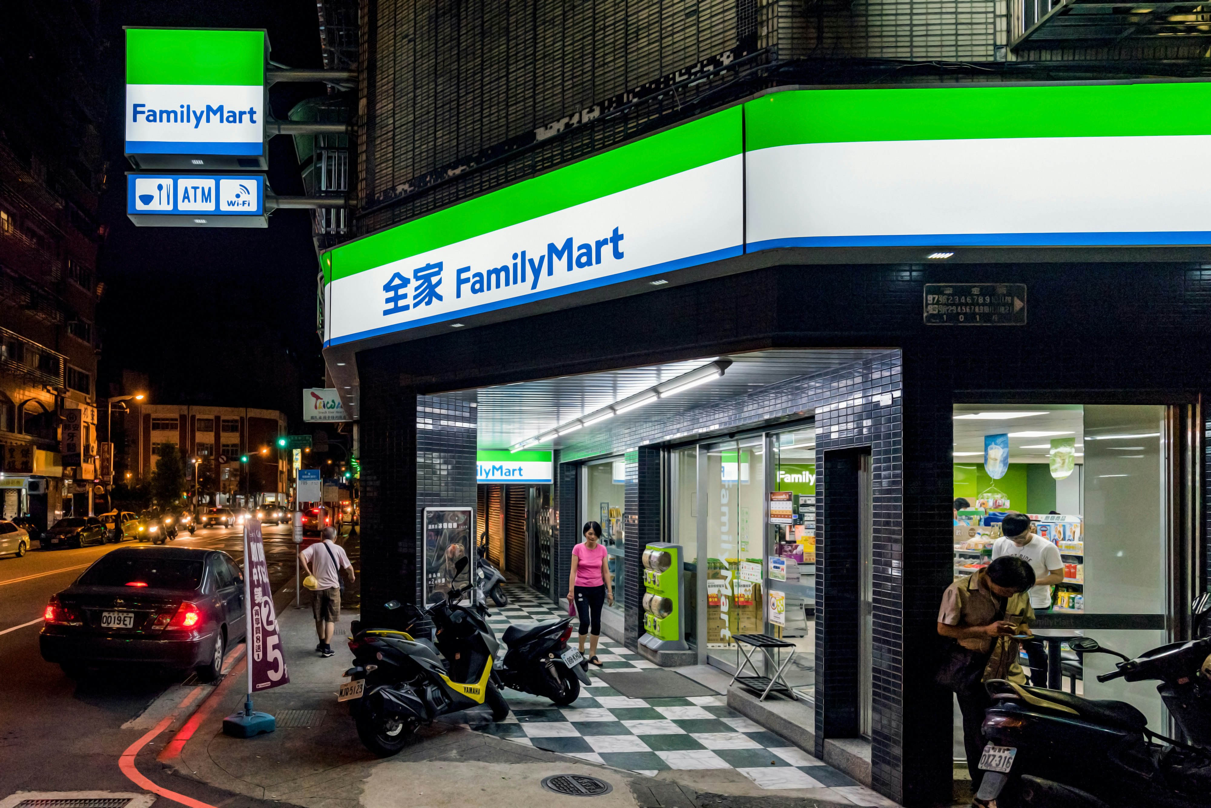 People outside of a brightly lit Family Mart convenience store in Taipei at night