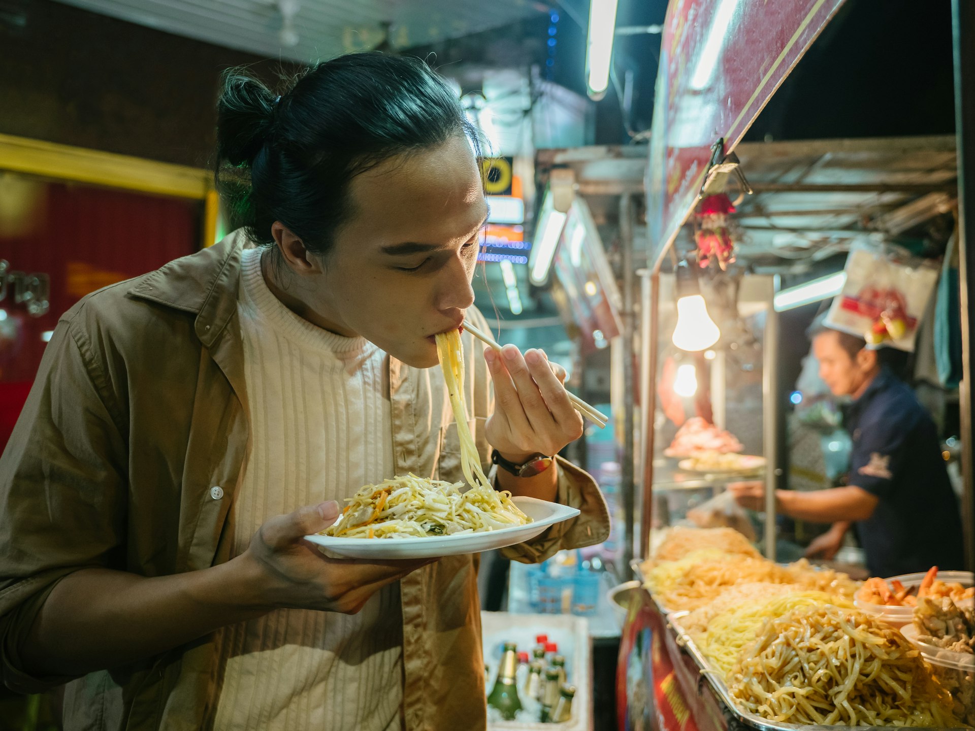 Young Asian man on Khao San Road, eating pat tai and enjoying various kinds of street food