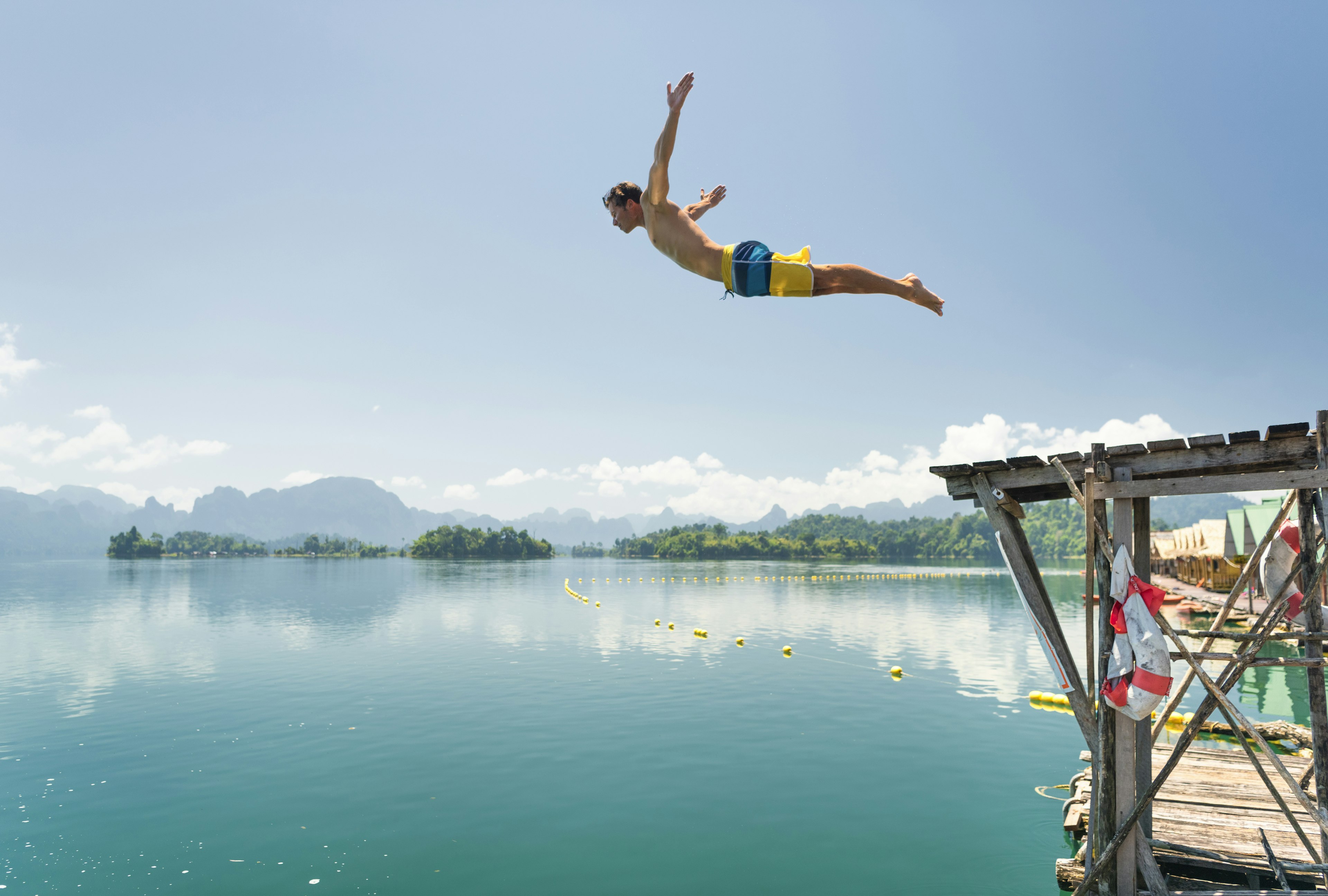 Athletic tourist jumping in the clear Lake Ratchaprapha, Khao Sok Nationalpark,