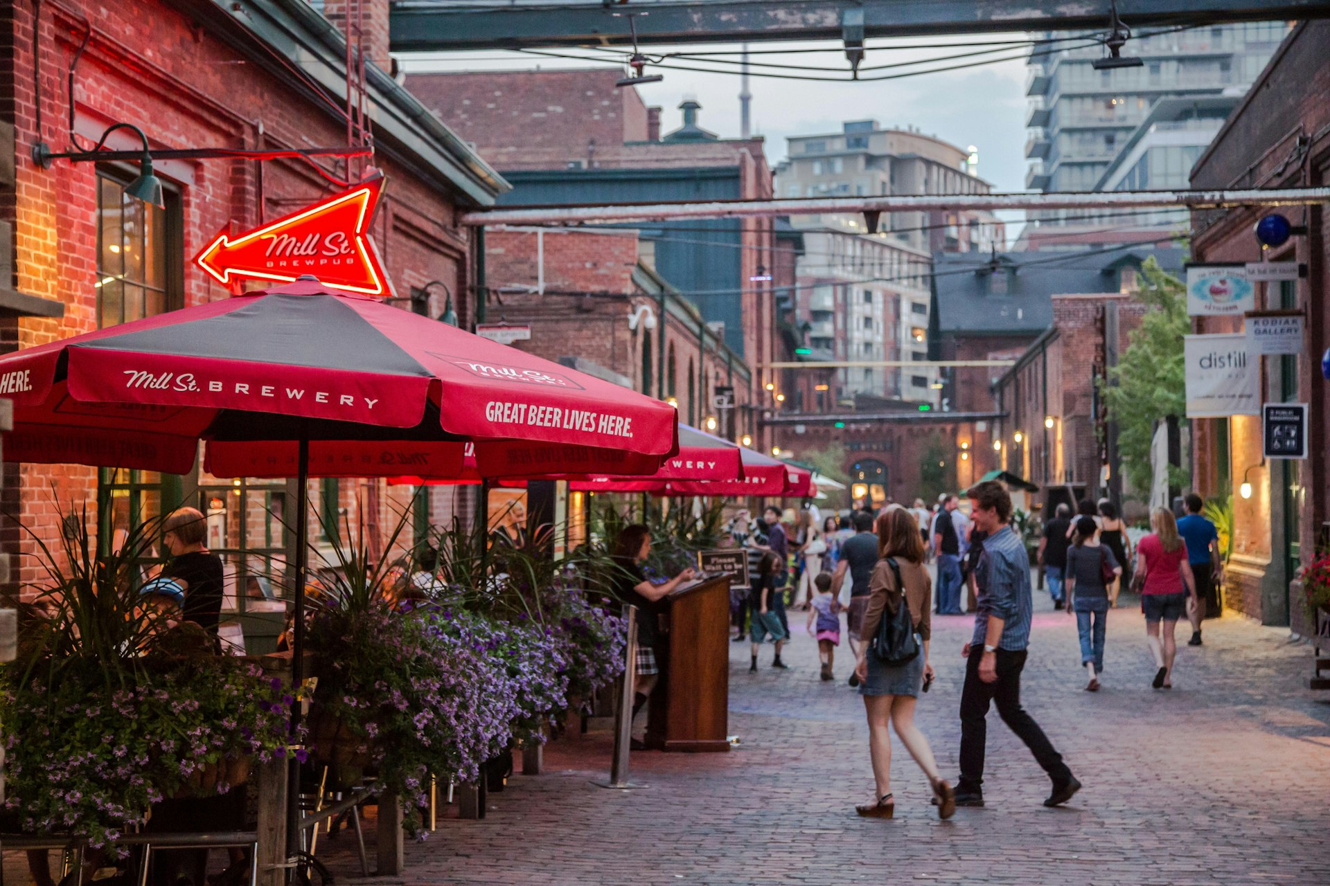 This photo shows a summer scene where district restaurants and bars have patio's set up allowing patrons to sit outdoors and enjoy a night out eating and people watching.