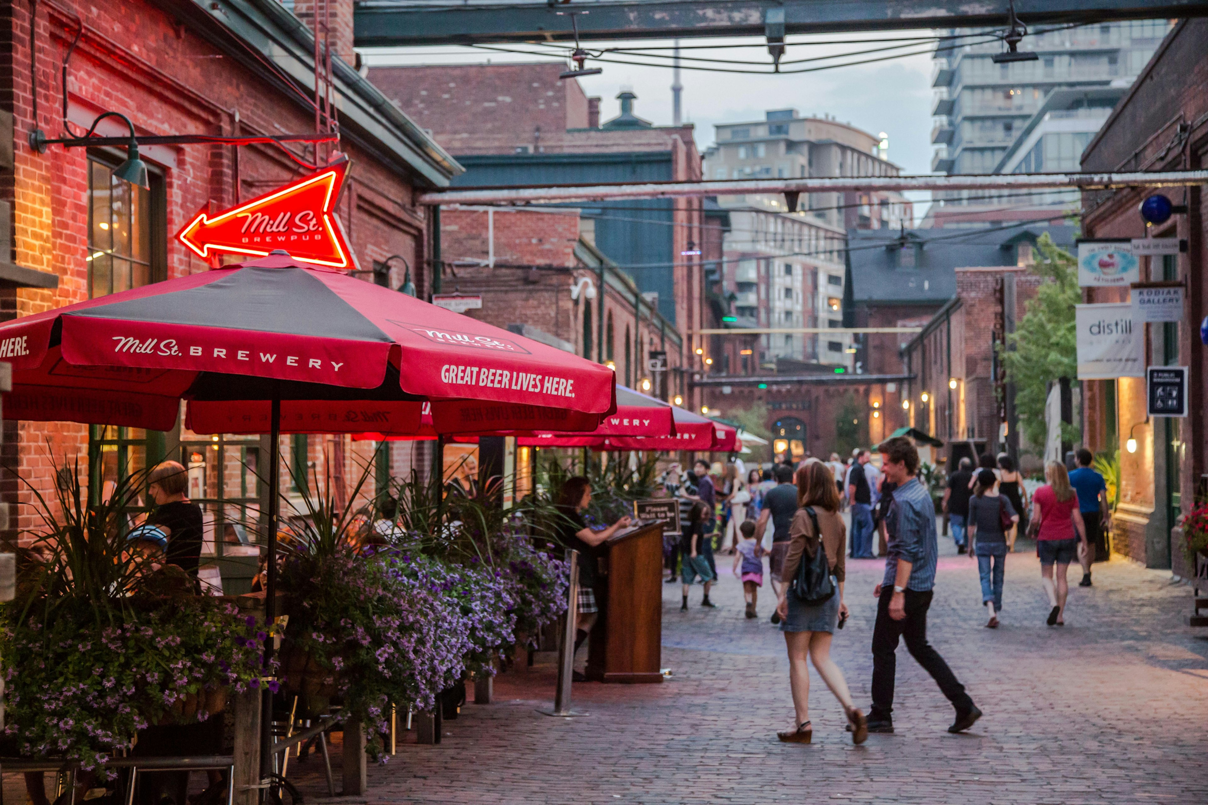 This photo shows a summer scene where district restaurants and bars have patio's set up allowing patrons to sit outdoors and enjoy a night out eating and people watching.