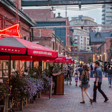Toronto, Ontario, Canada - July 13, 2012: The Distillery District, in Toronto, Ontario, is named after this area's history in distilling spirits. After falling into a state of disrepair by the turn of the millennium, efforts began to redevelop the area and create a destination for locals and tourists alike. The old brick Victorian structures were converted into retail, commercial and residential space. Many galleries, bars, restaurants and cafes line the area. It hosts various cultural events and has become a 'must see' district for those visiting Toronto...This photo shows a summer scene where district restaurants and bars have patio's set up allowing patrons to sit outdoors and enjoy a night out eating and people watching. The roads here are for pedestrians only.