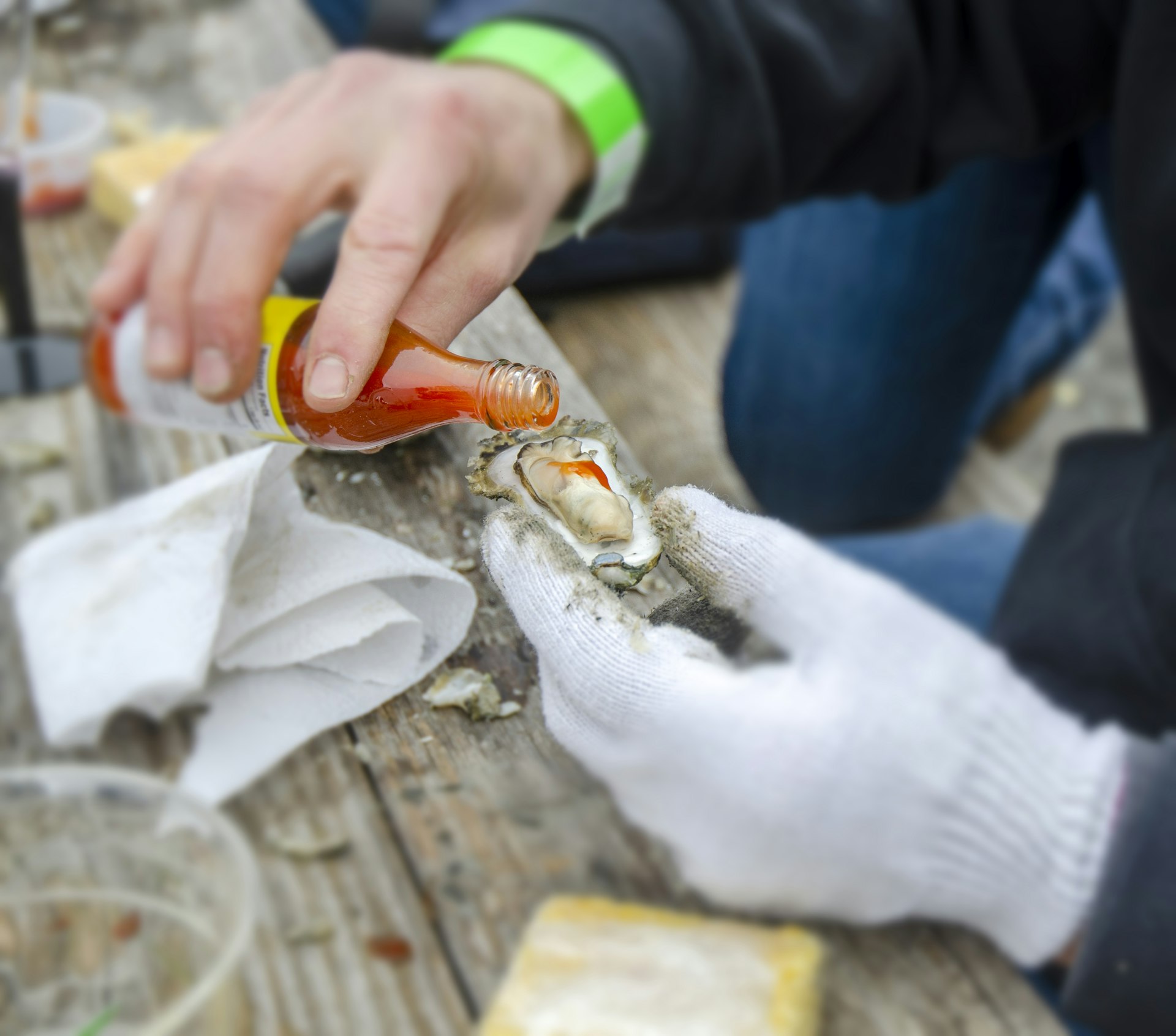 A person holding an oyster pours some hot sauce onto it at the table