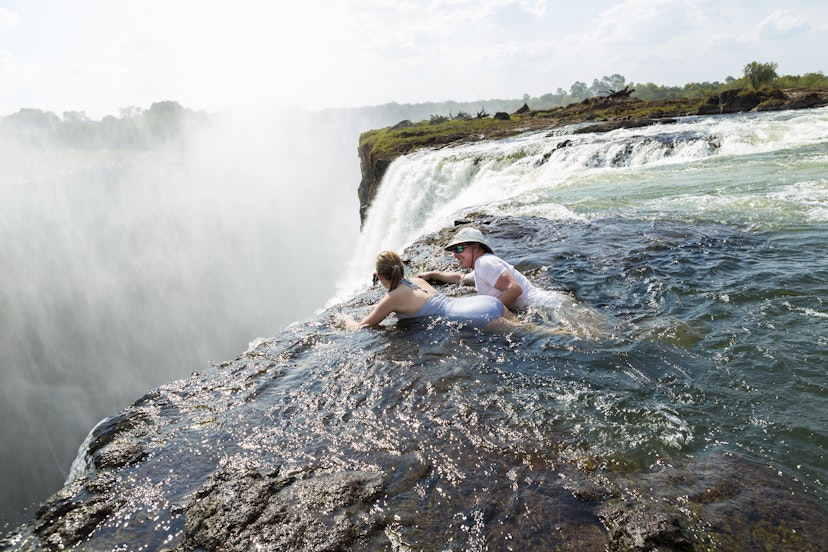 Man and a girl, father and daughter in the water of the Devil's Pool on the edge of Victoria Falls, mist rising from the falling water.