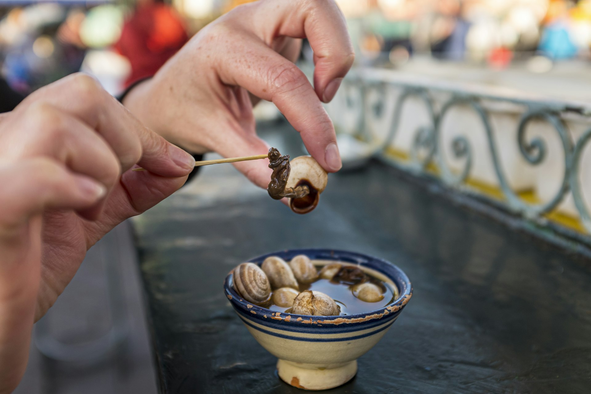 Woman extracting a snail from its shell in a bowl of soup in Morocco