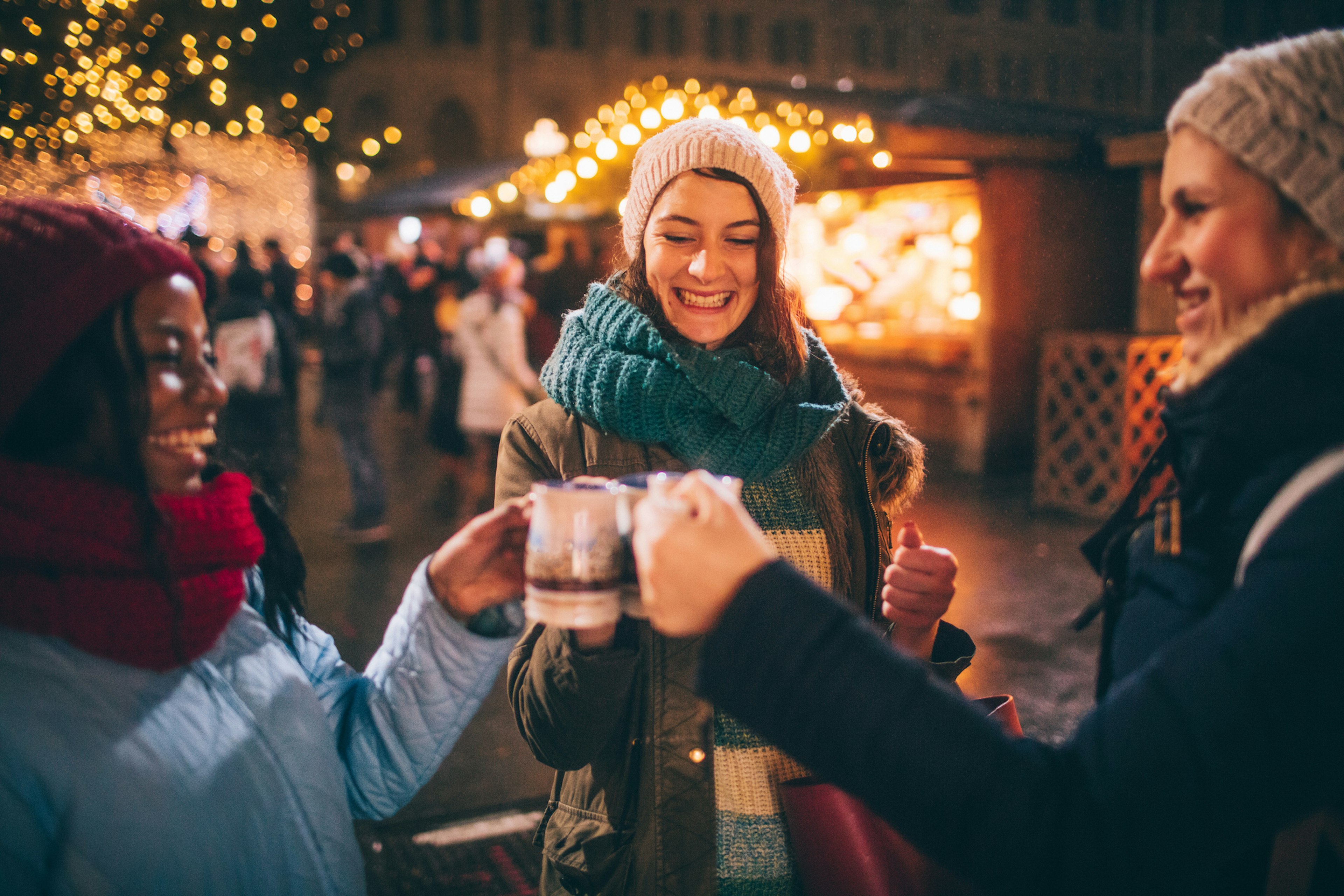 Three women raising a toast and enjoying mulled wine at a Christmas market