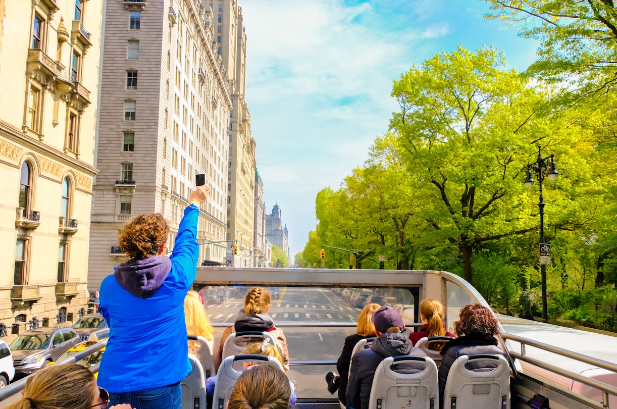 Tourists enjoying views of New York City from top of open roof bus in spring; woman in blue is taking photos with her smartphone; Shutterstock ID 1399814936; your: Zach Laks; gl: 65050; netsuite: Online Editorial; full: Discover