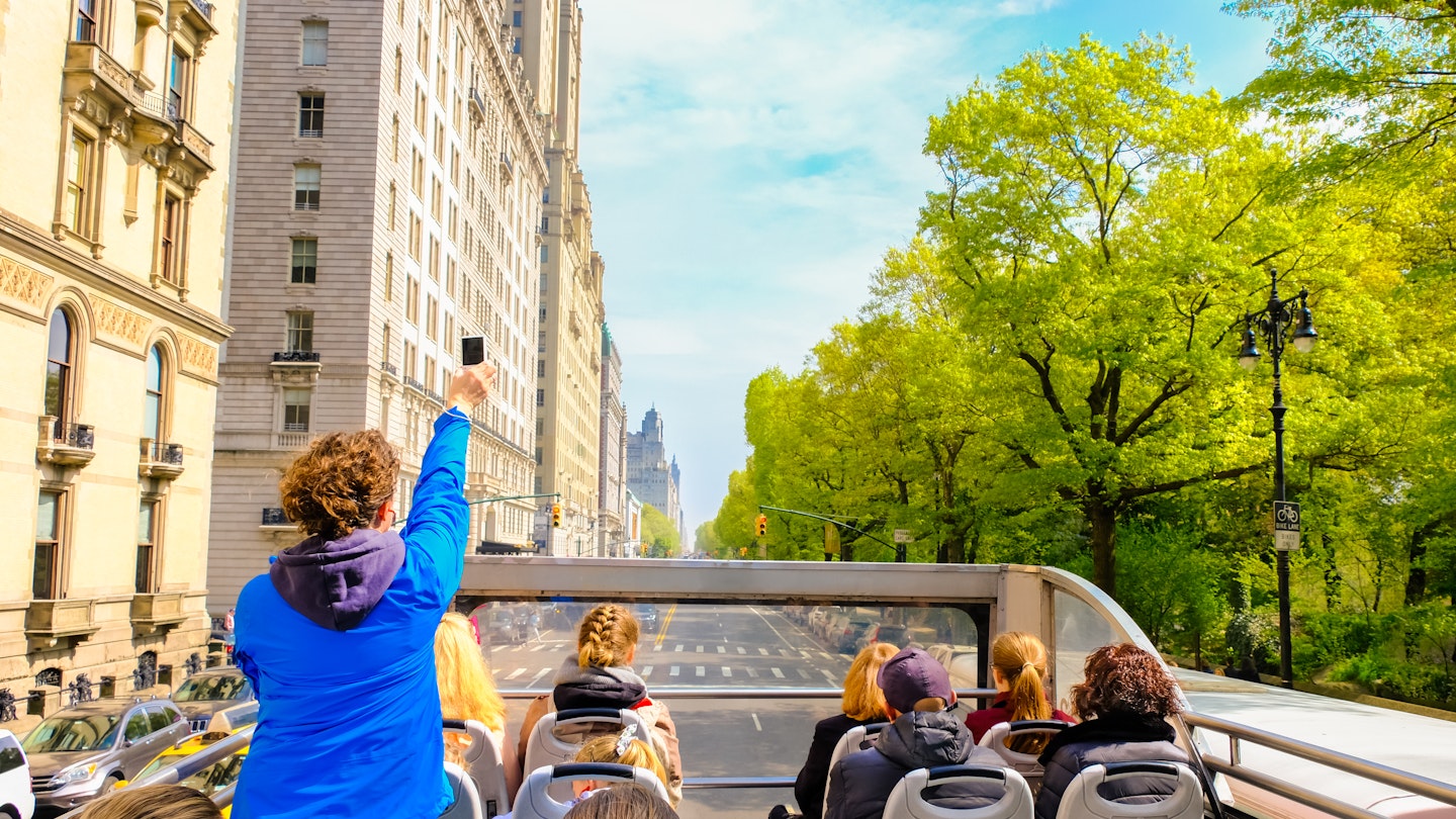 Tourists enjoying views of New York City from top of open roof bus in spring; woman in blue is taking photos with her smartphone; Shutterstock ID 1399814936; your: Zach Laks; gl: 65050; netsuite: Online Editorial; full: Discover