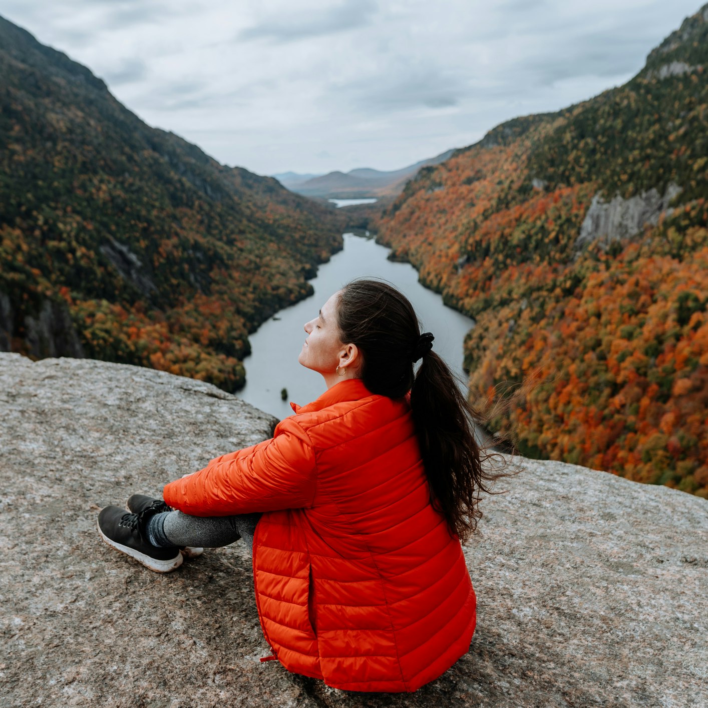 Hiking in the Adirondack Mountain Indian Head Trail in the fall
A woman sits on a rock overlooking a river and the Adirondacks mountains in the fall