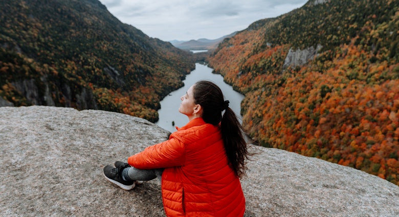 Hiking in the Adirondack Mountain Indian Head Trail in the fall
A woman sits on a rock overlooking a river and the Adirondacks mountains in the fall