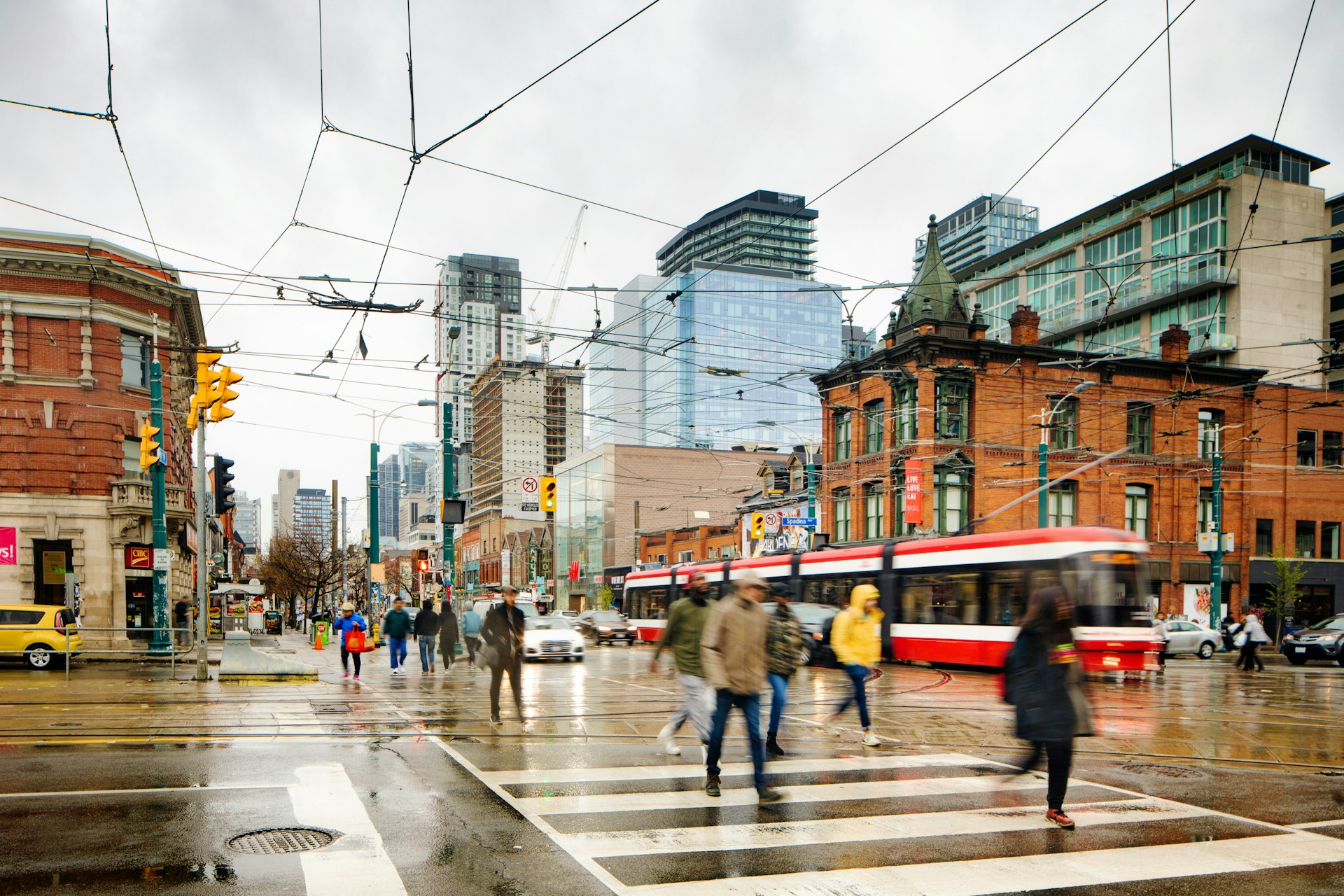 People cross a busy street in Toronto on a cloudy day