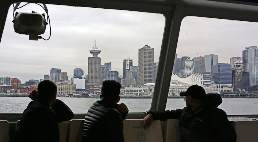 SeaBus passengers view downtown Vancouver and Burrard Inlet on the way to Lonsdale Quay in North Vancouver. Urban skyline shows the waterfront in winter.